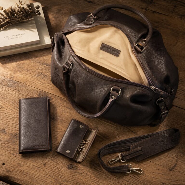 Sacs et accessoires en cuir Arthur & Aston élégamment disposés sur une table en bois, éclairés par une lumière directionnelle chaude créant des ombres douces.