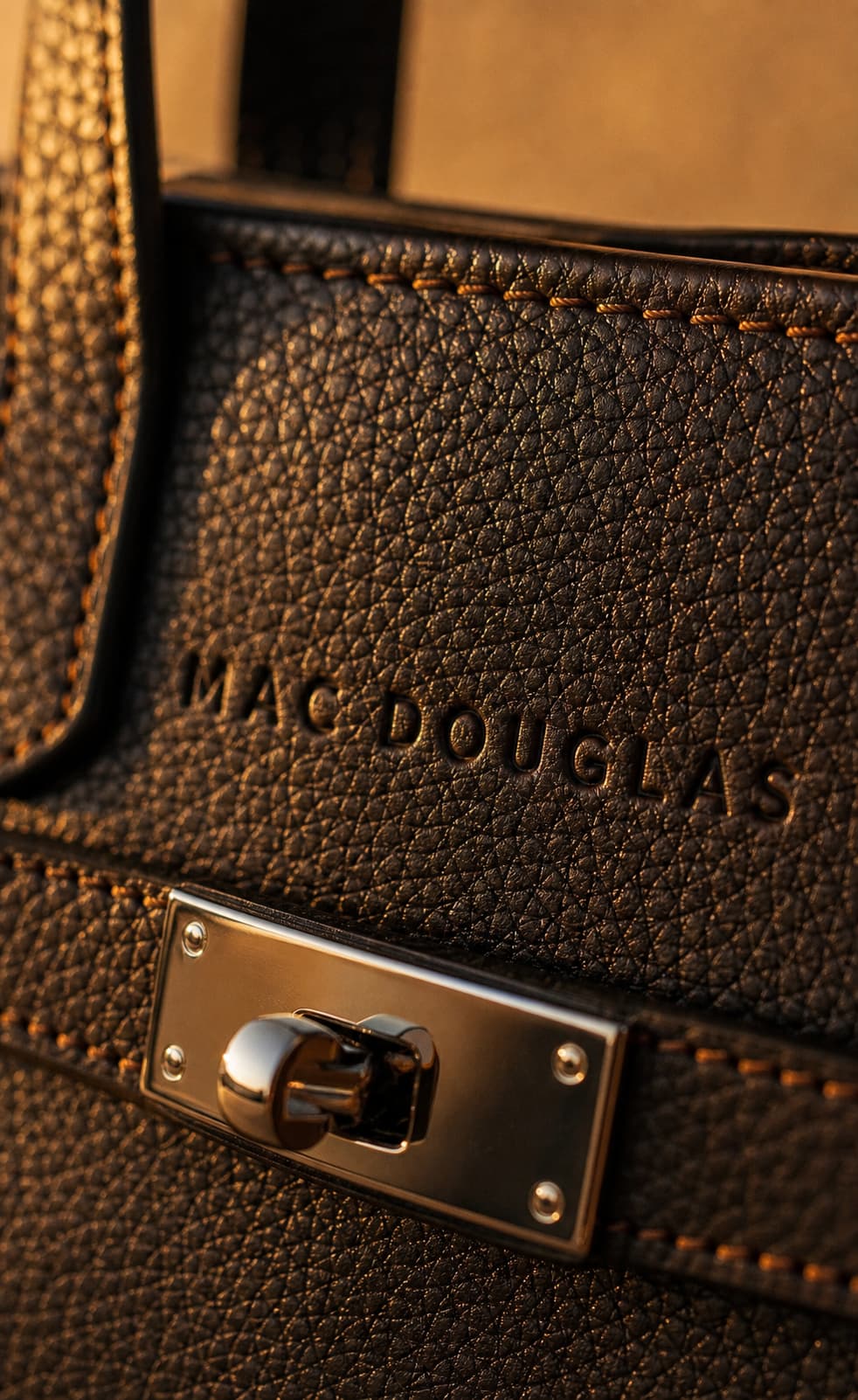 Gros plan du logo Mac Douglas embossé sur du cuir véritable, montrant le grain et les coutures précises sous une lumière chaude.