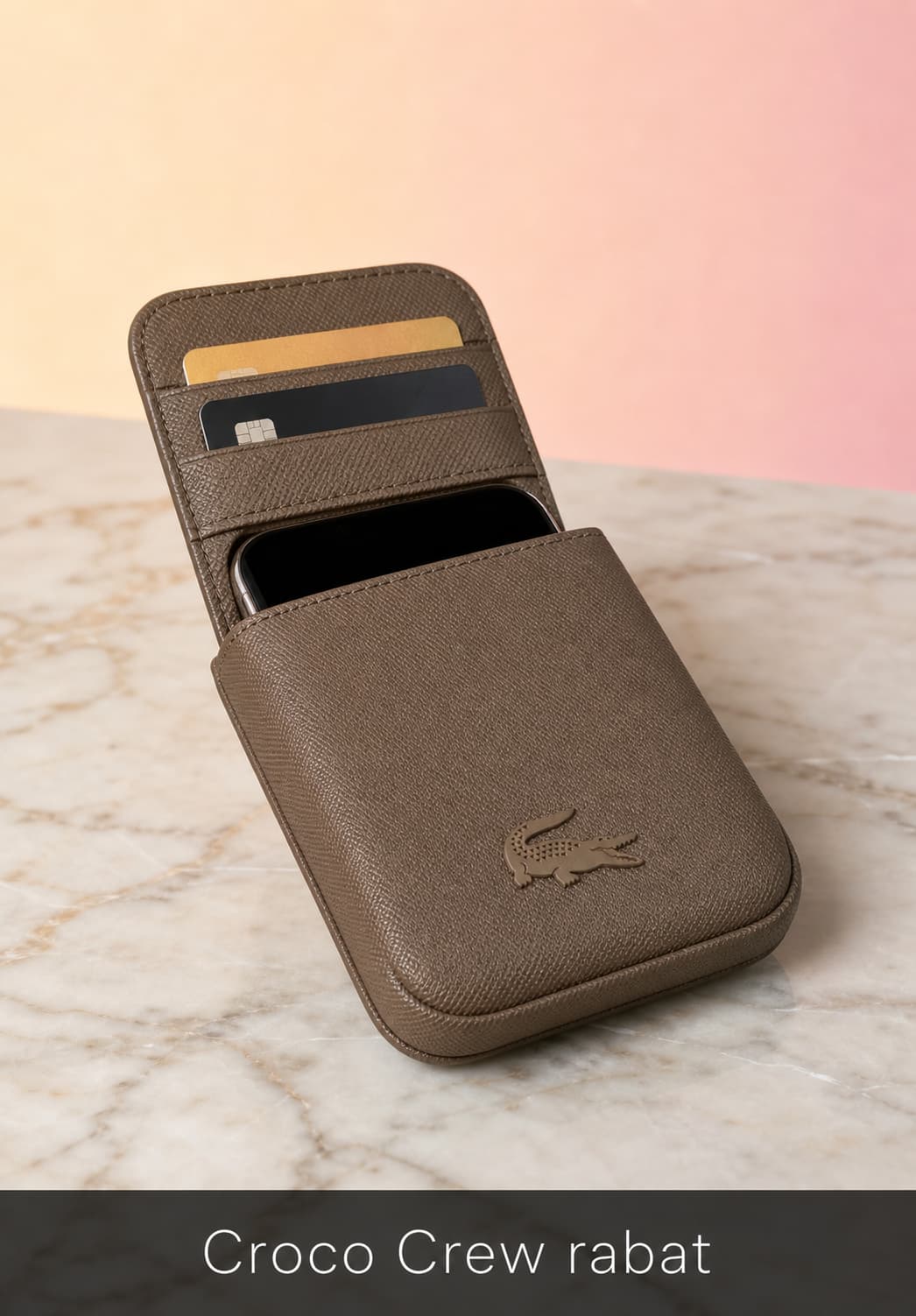 Pochette smartphone Lacoste Croco Crew en cuir grainé ouverte sur une surface en marbre, dévoilant un smartphone et deux cartes de crédit, avec un badge crocodile en relief sur le rabat, éclairage doux de studio et fond dégradé crème à rose.