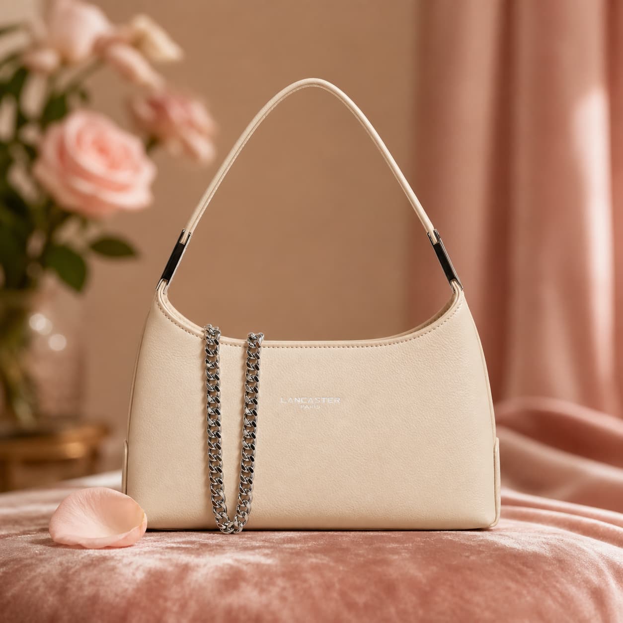 Petit sac Lancaster Suave Ace en cuir grainé crème sur fond de velours, avec chaîne délicate, logo discret et pétale de rose, dans une lumière douce et romantique.