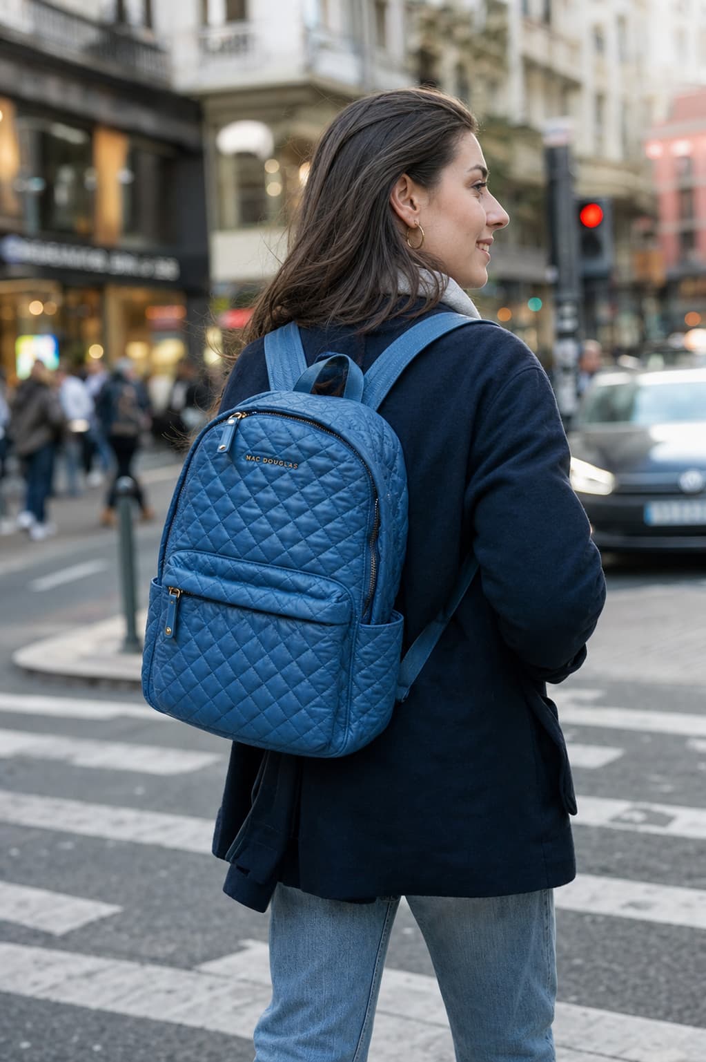Une femme portant le sac à dos matelassé Manchester MIAMI de Mac Douglas marche dans une rue urbaine, arrière-plan flou, mise au point sur la texture du sac.