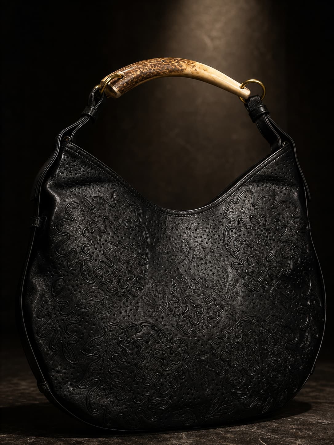 Sac Saint Laurent Mombasa en cuir noir avec une poignée en forme de corne, silhouette incurvée, sur fond sombre aux ombres dramatiques.