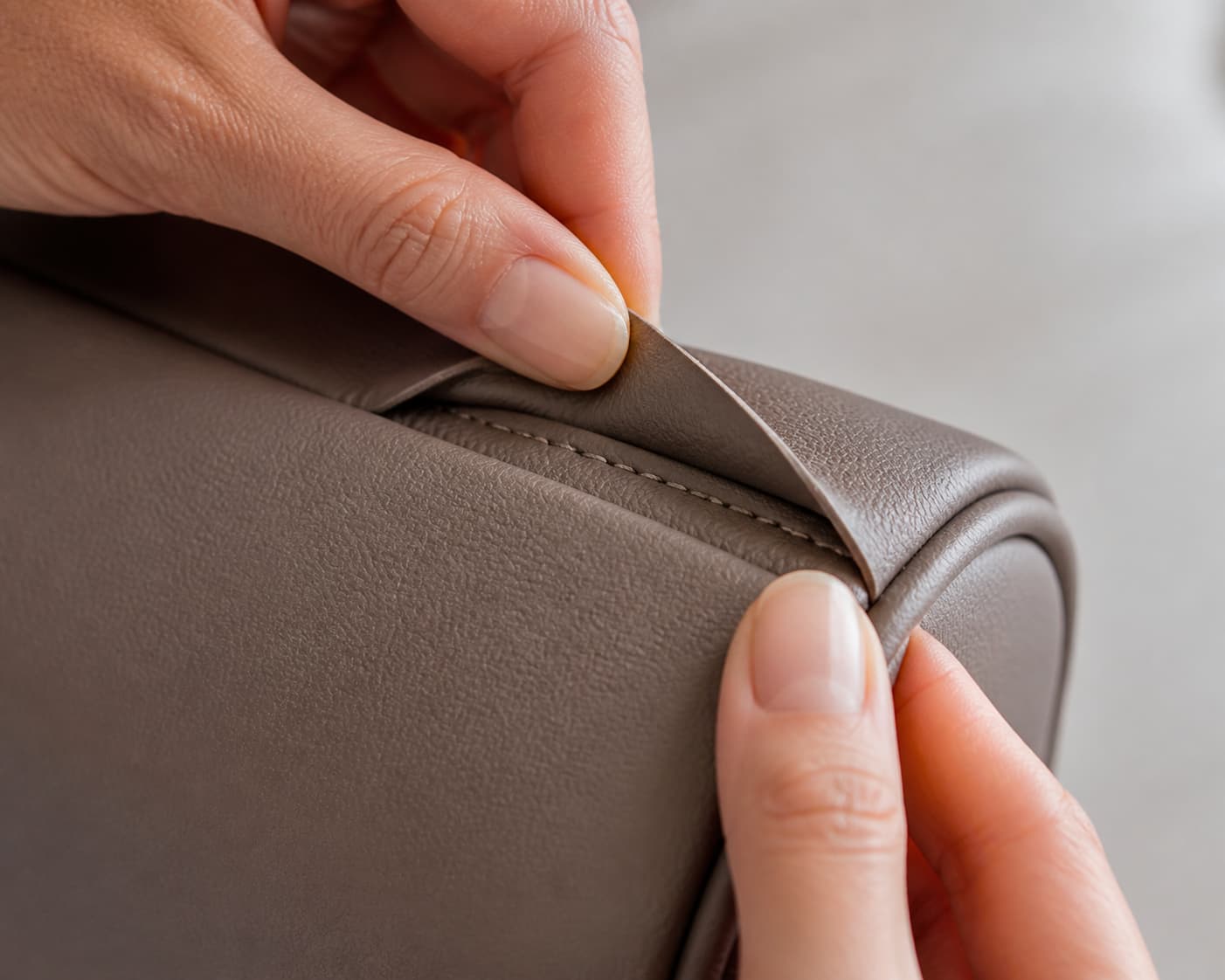 Mains inspectant de près les coutures et l’angle d’un sac en cuir vegan, avec le revêtement soulevé.