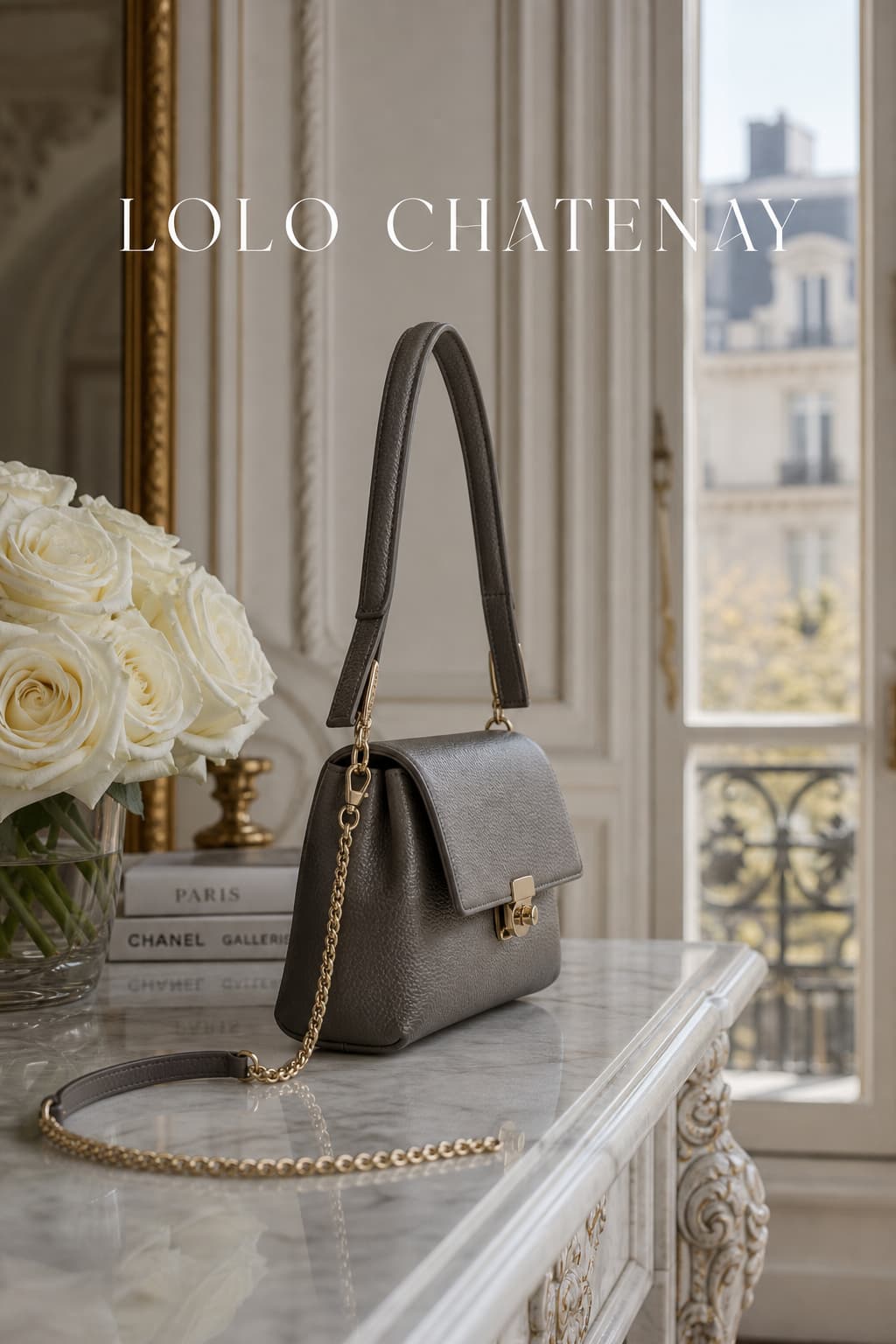 Sac à main structuré LOLO CHATENAY en cuir gris grainé avec fermoir doré, posé sur une console en marbre à côté de roses blanches dans un appartement parisien lumineux, avec le texte