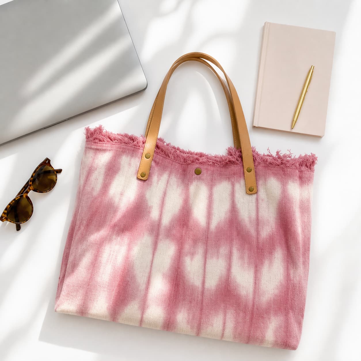 Un sac cabas rose pastel de la marque Fuchsia Paris repose à plat sur un bureau blanc, entouré d’un ordinateur portable, d’un carnet et de lunettes de soleil.
