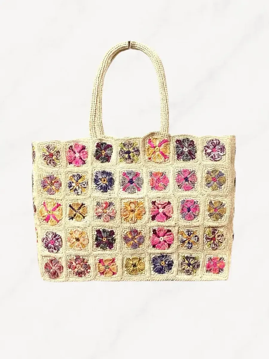 Sac à main en crochet Fuchsia Paris en raphia naturel, posé sur une jetée en bois au bord de la mer sous une lumière chaude avec flou d’arrière-plan.